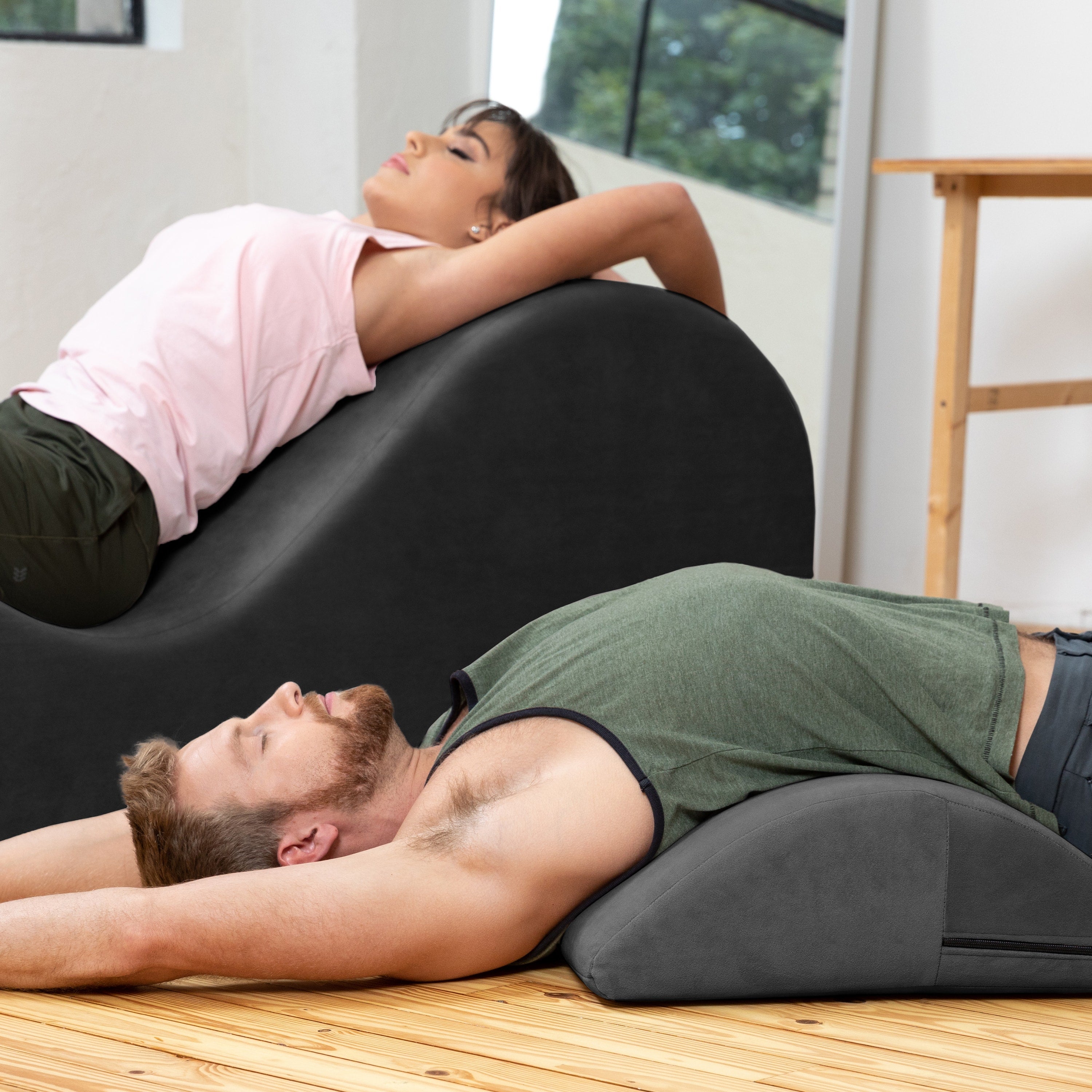 Two people relaxing on contoured massage chairs in a bright indoor space with wood flooring.