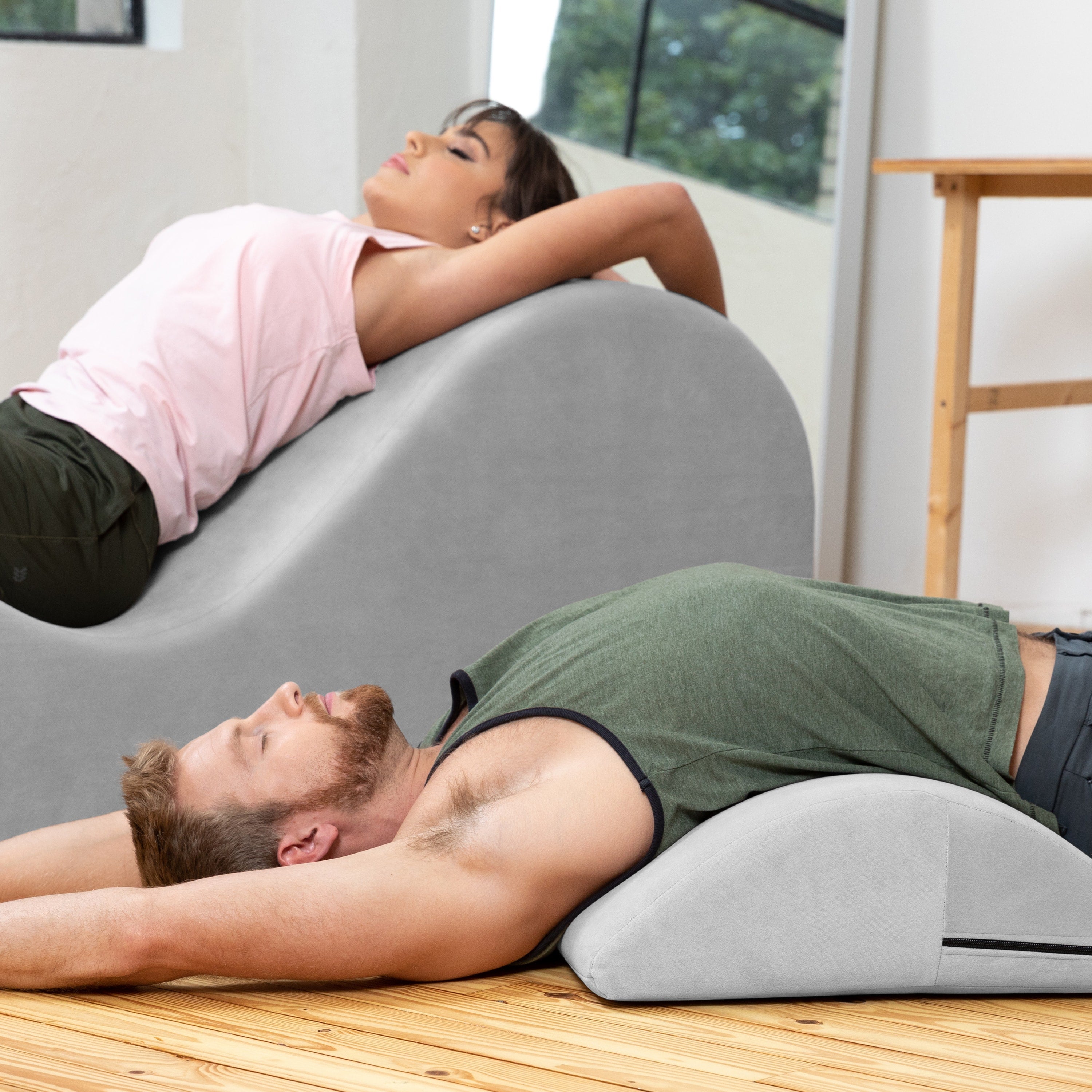 Two people using a curved chaise on a wooden floor with a neutral background