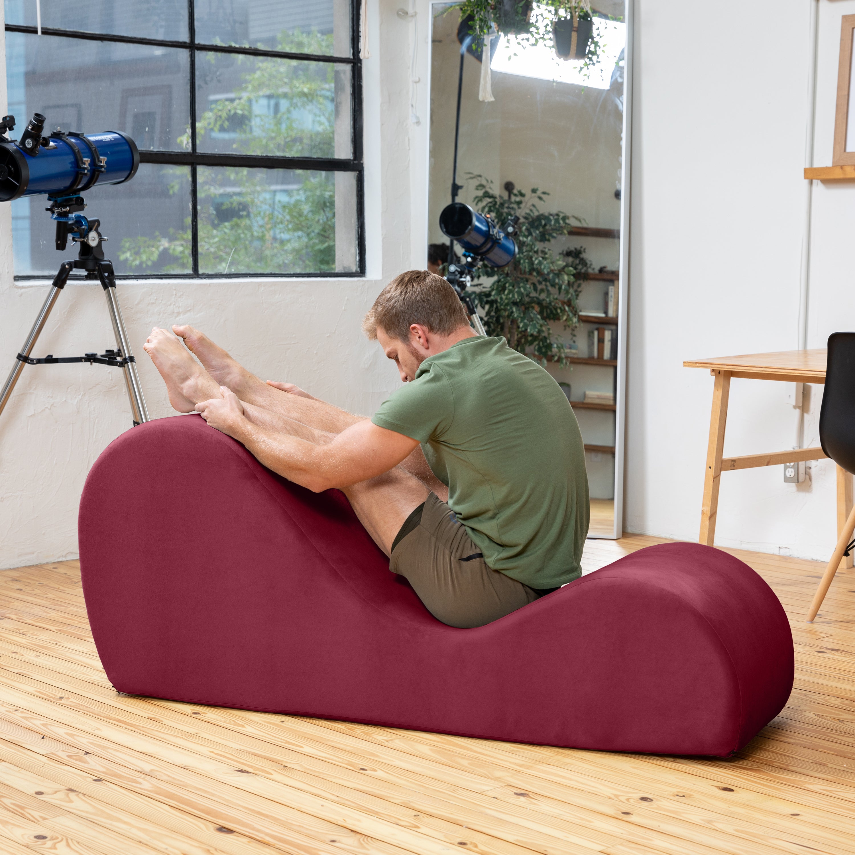 Person using a red exercise device in a room with a telescope and plants.