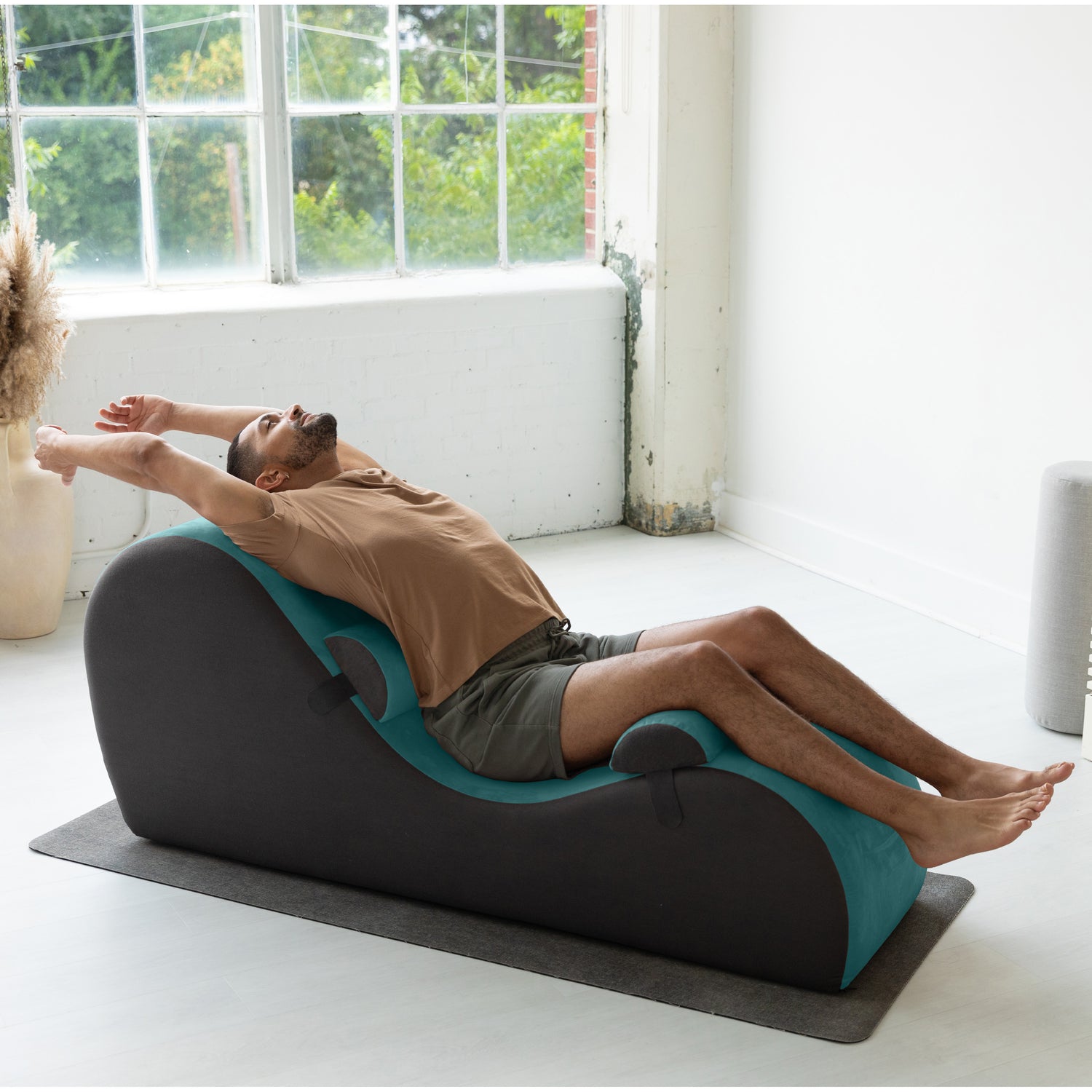 Person using a massage roller chair in a bright room with large windows.