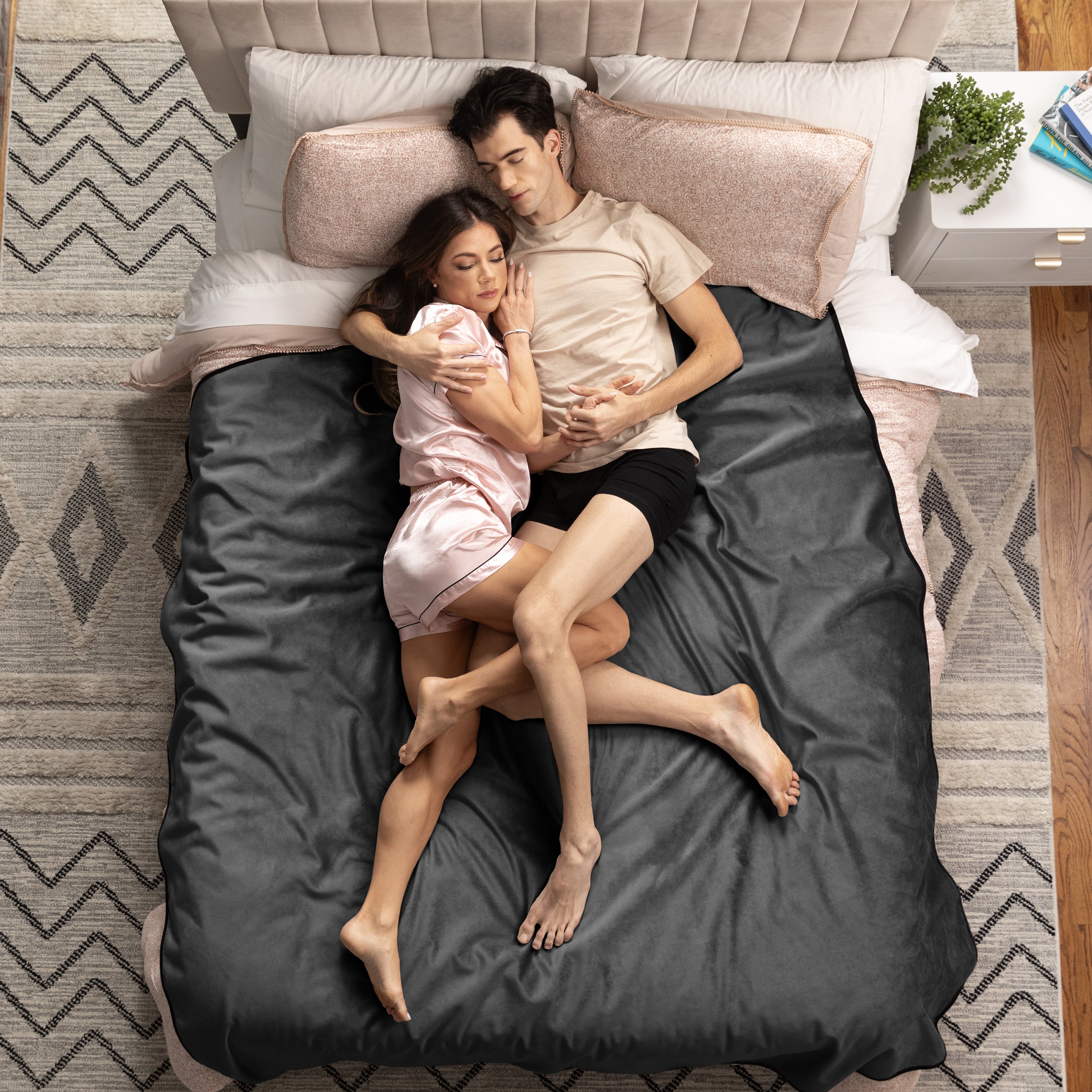 Couple lying on a bed with gray bedding in a cozy bedroom setting.