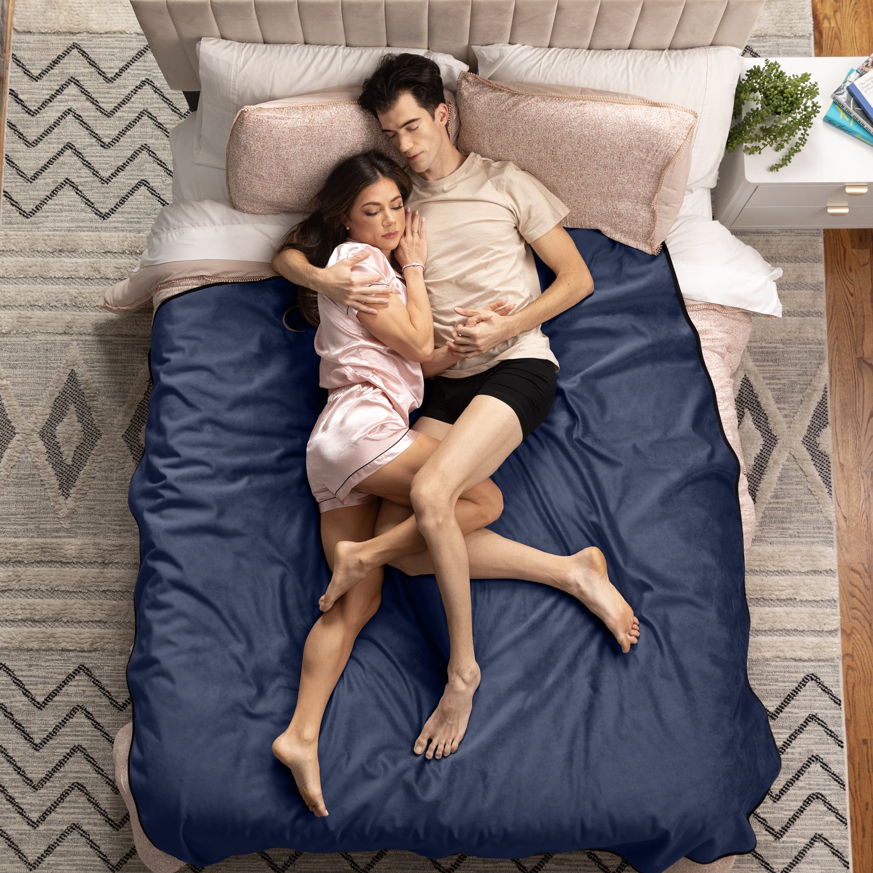 Couple lying in bed under a blue throw in a bedroom setting.