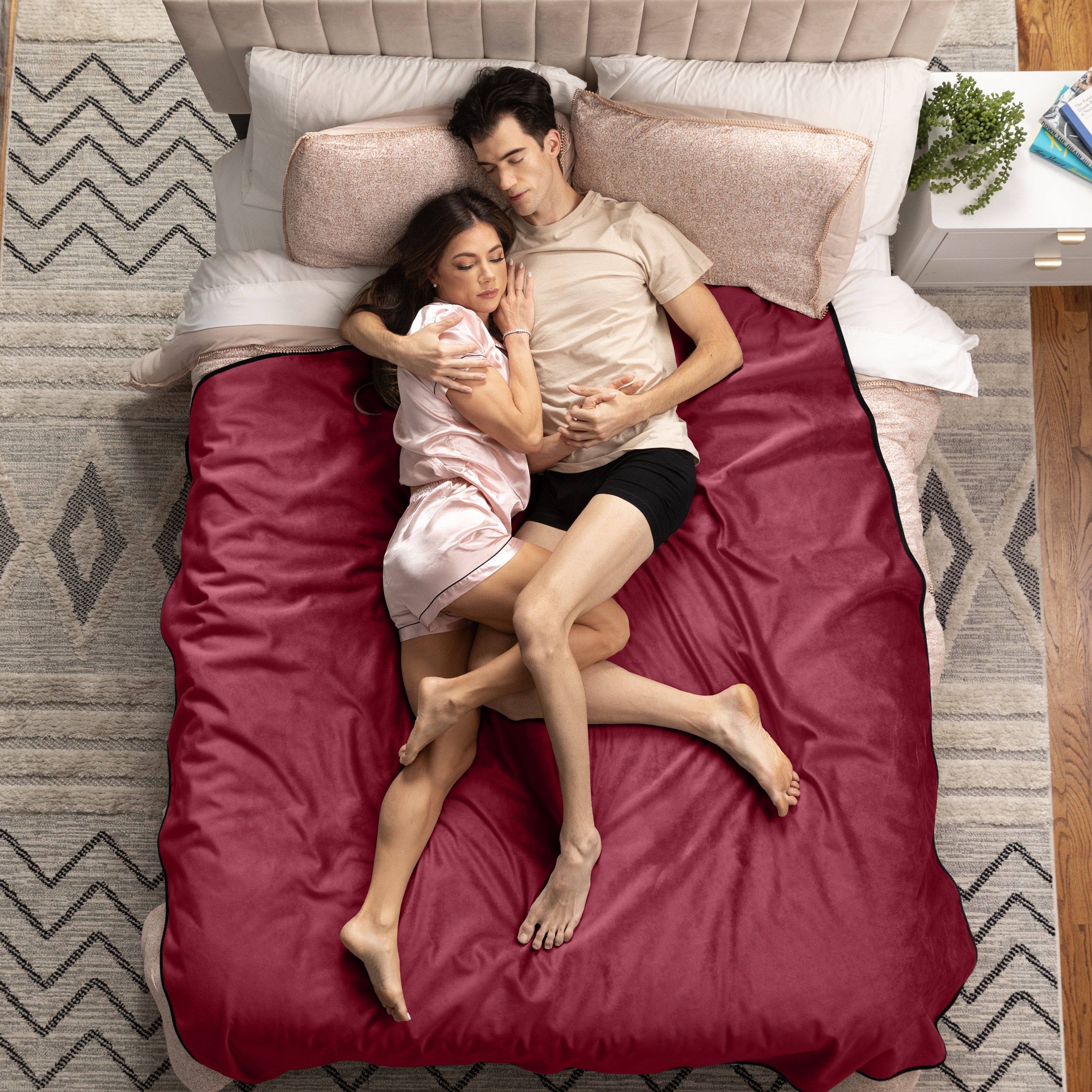 Couple lying on a bed with red bedding in a cozy bedroom setting.