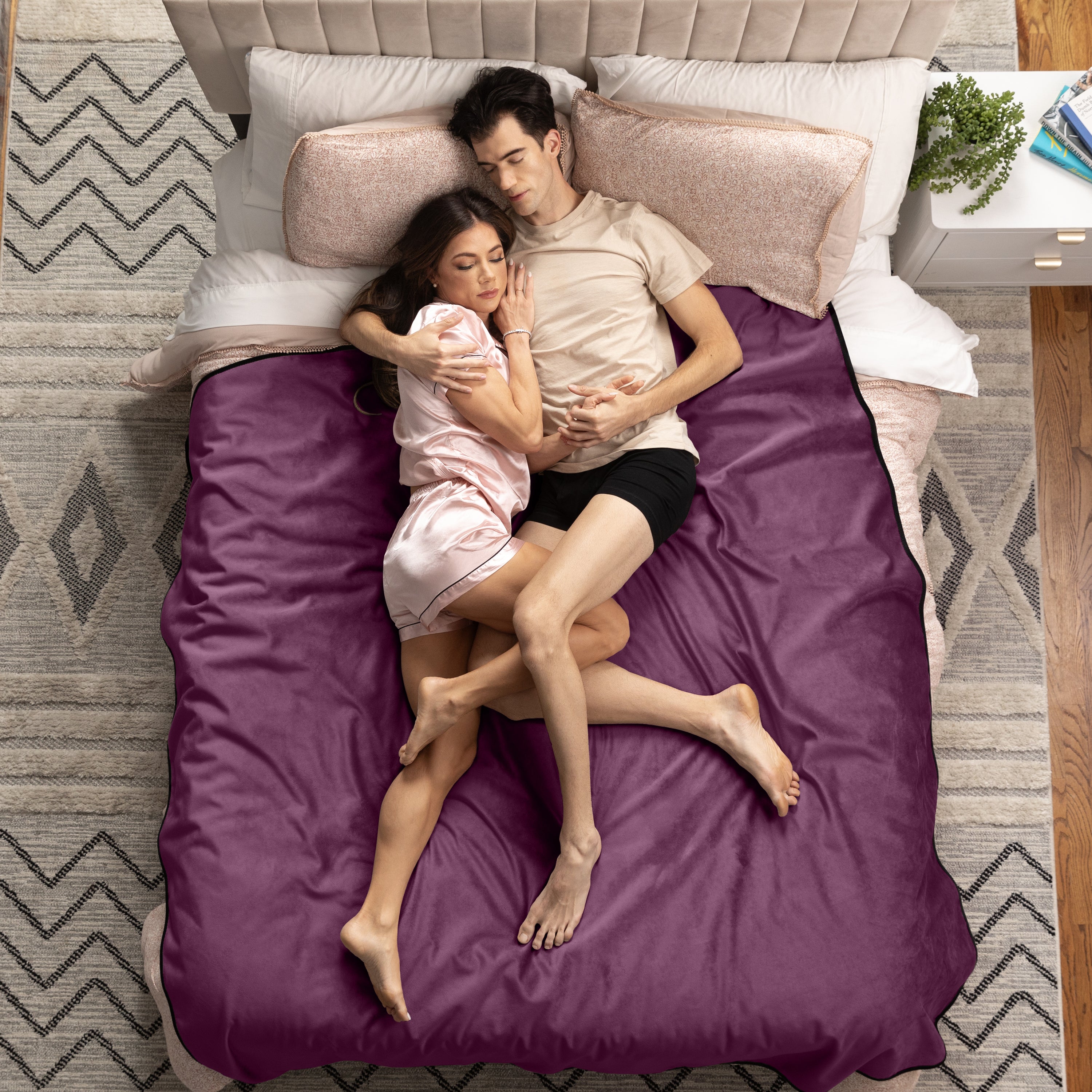 Couple lying in bed under a purple throw in a bedroom setting.