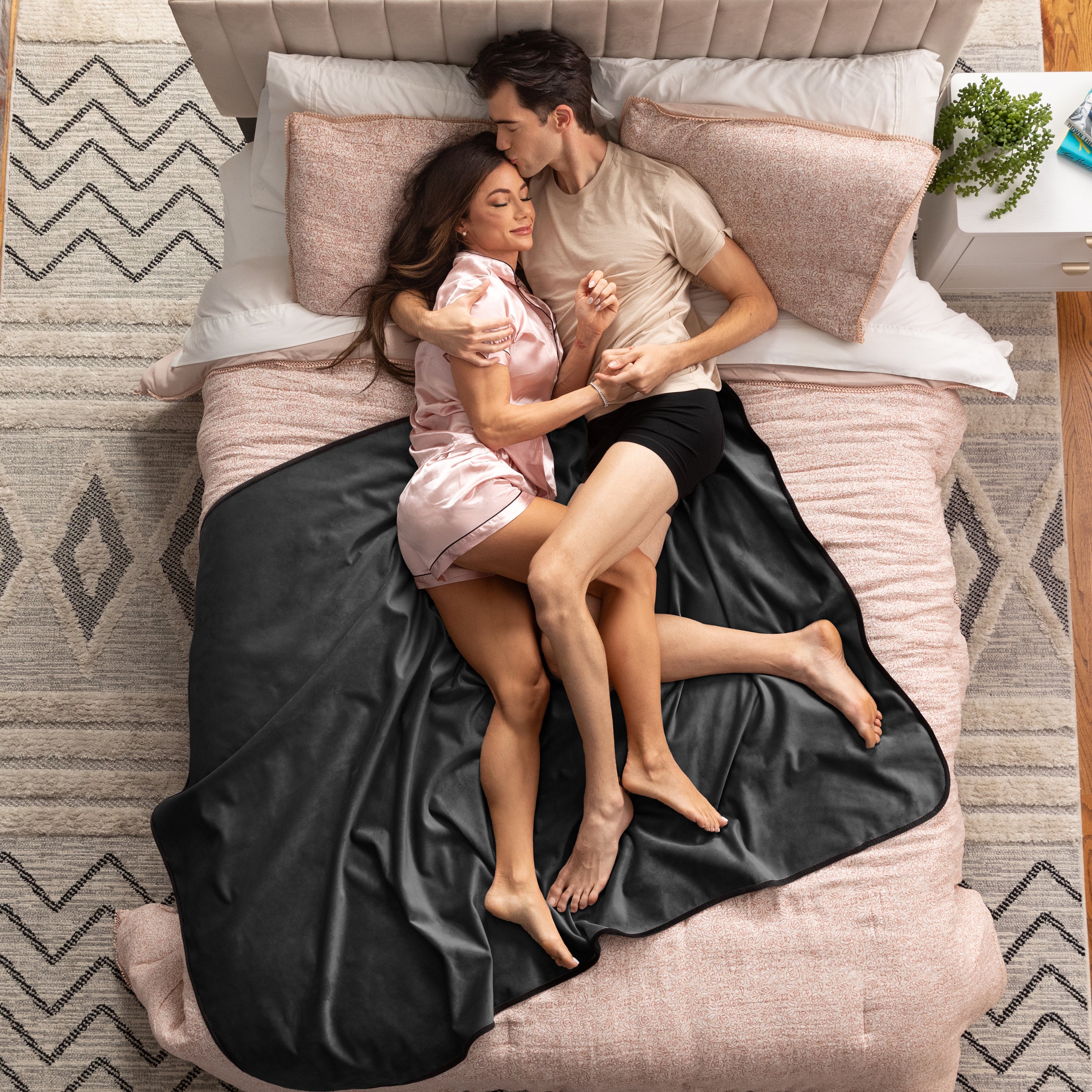Couple lying on a bed under a black blanket in a bedroom setting.