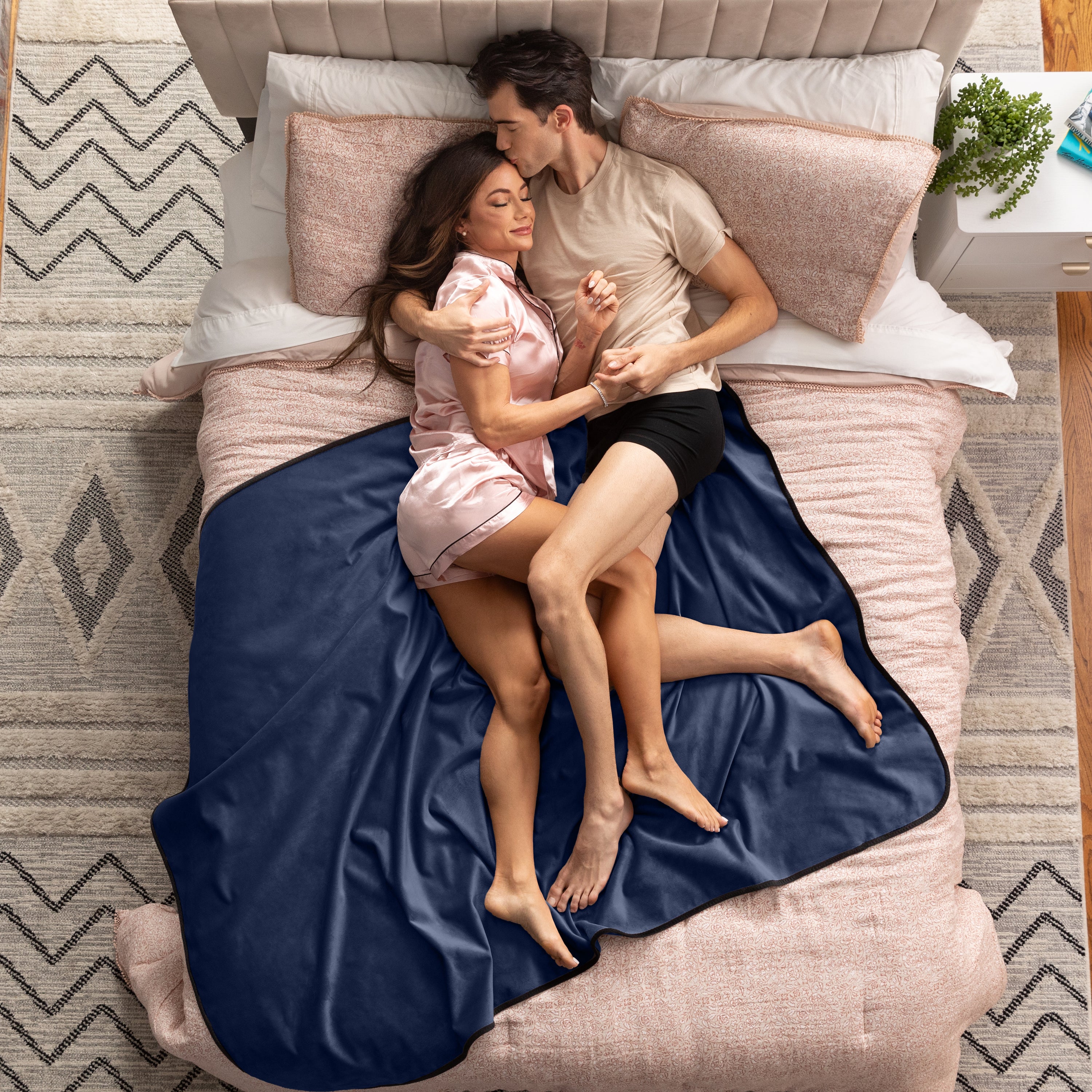 Couple lying on a bed under a blue blanket in a bedroom setting.