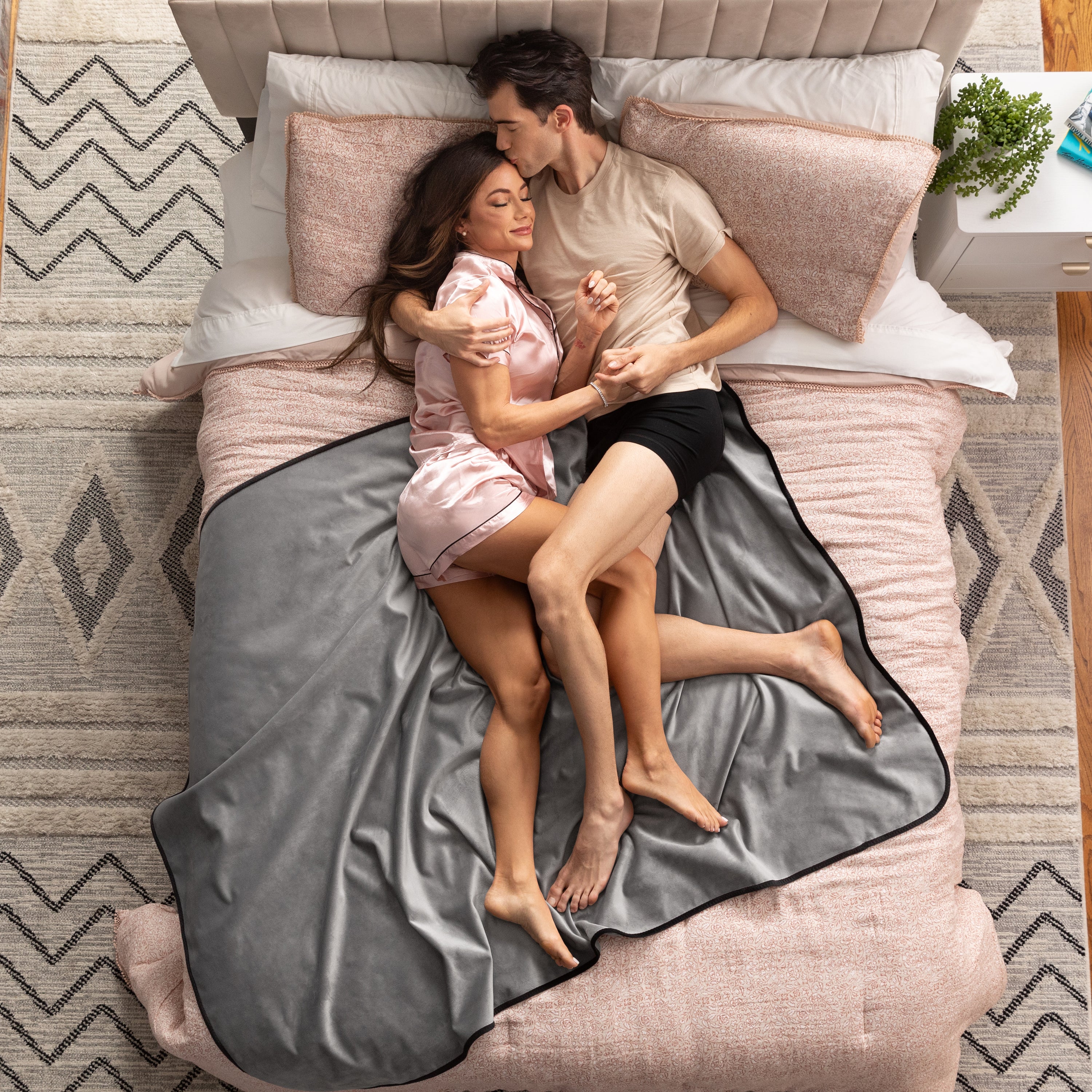 Couple lying on a bed under a gray blanket in a bedroom setting.