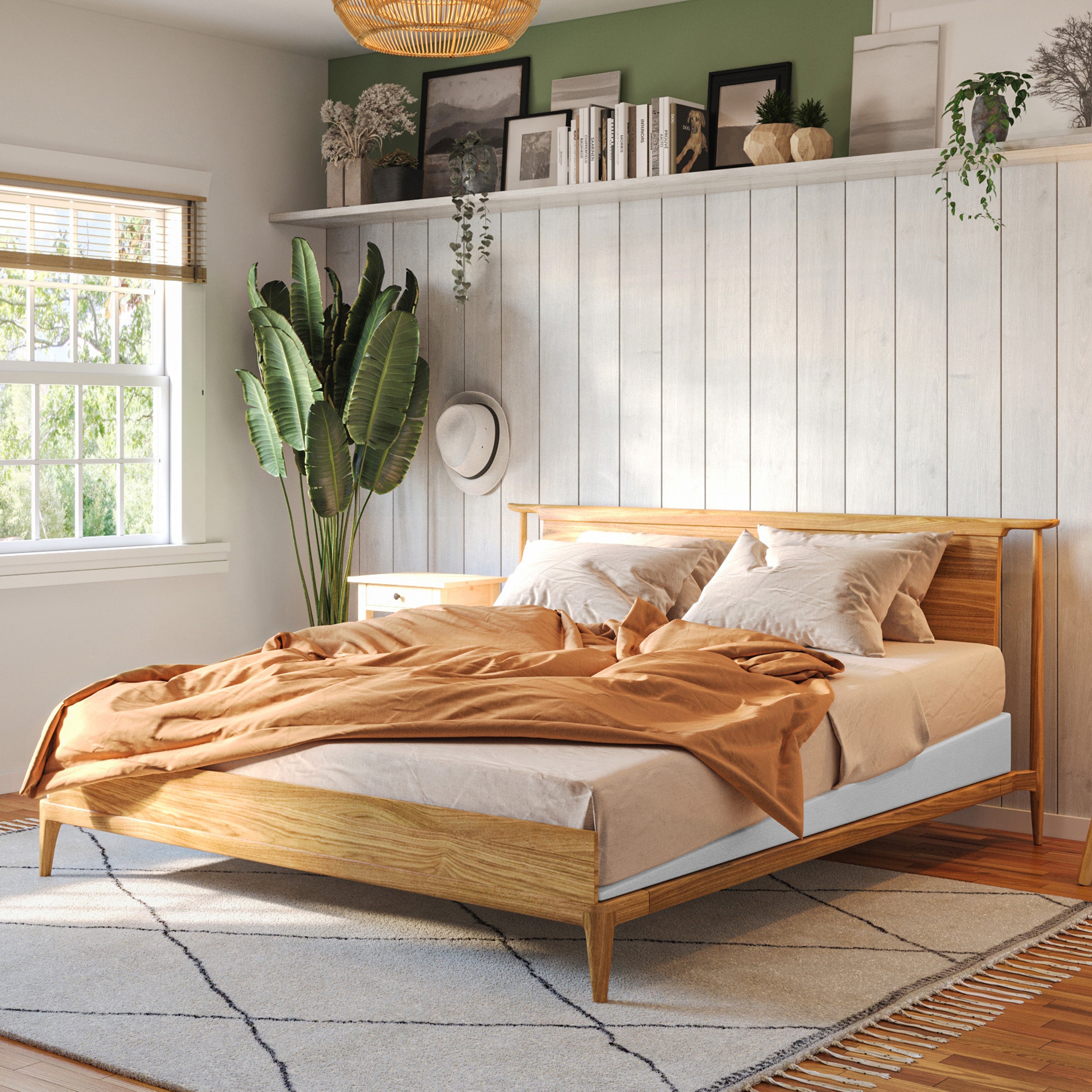 A light natural wood bed frame with a low-profile platform design, styled with beige and white bedding and a rust-orange throw blanket in a bright, modern bedroom.