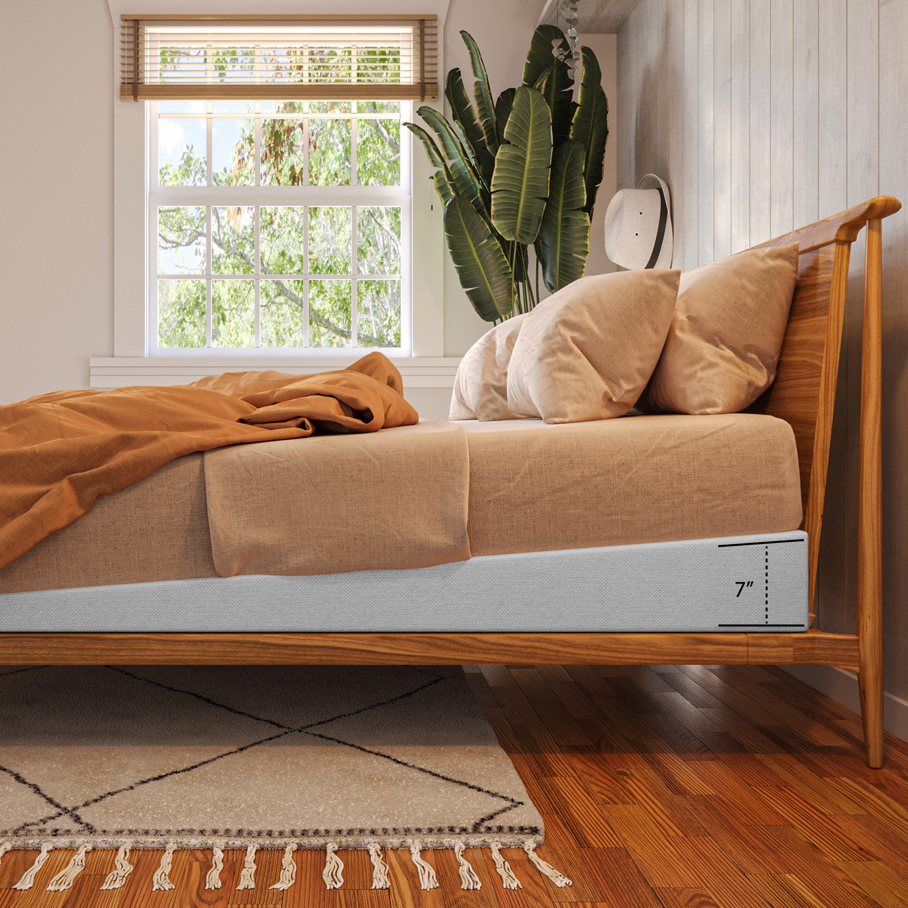 A wooden bed frame with a light beige upholstered mattress and matching pillows, styled in a bright bedroom with a window, plant, and wood floor. A white side panel shows a printed '7"' measurement marker.